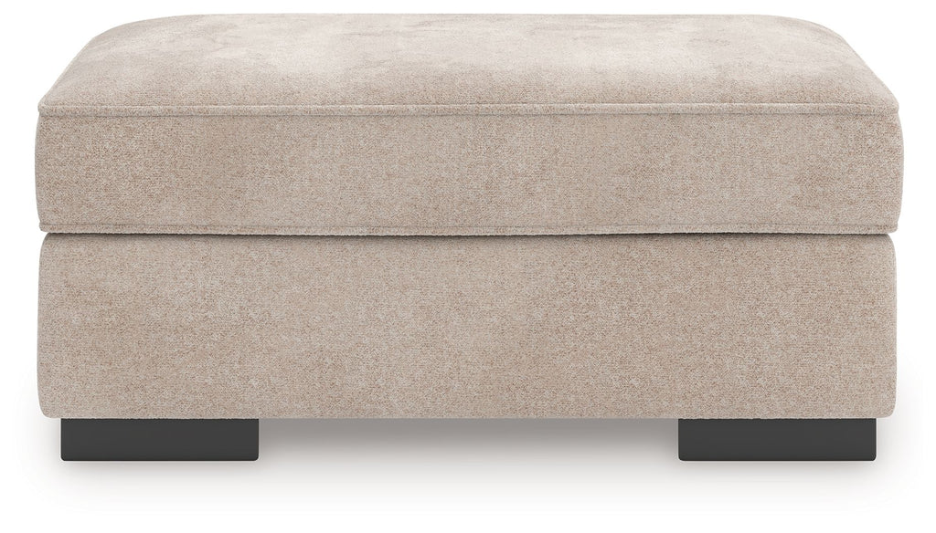 Taupe upholstered ottoman with low rectangular sides and black legs