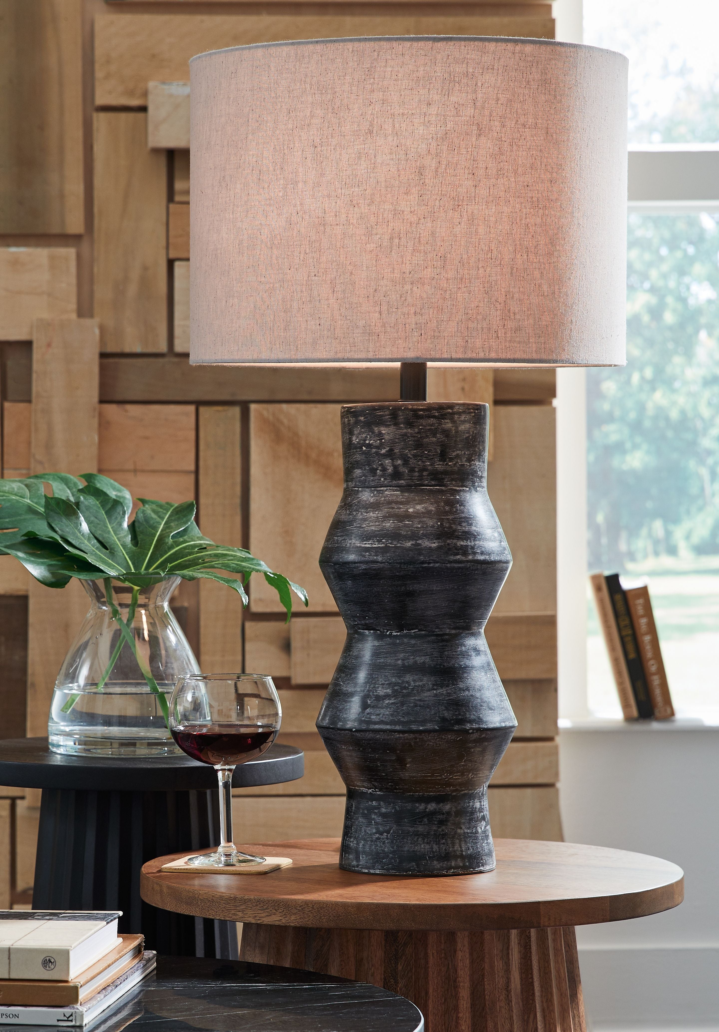 Distressed black table lamp with beige drum shade and tiered column base.