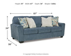 Blue upholstered sofa shown from side angle with four pillows and patterned accent throws