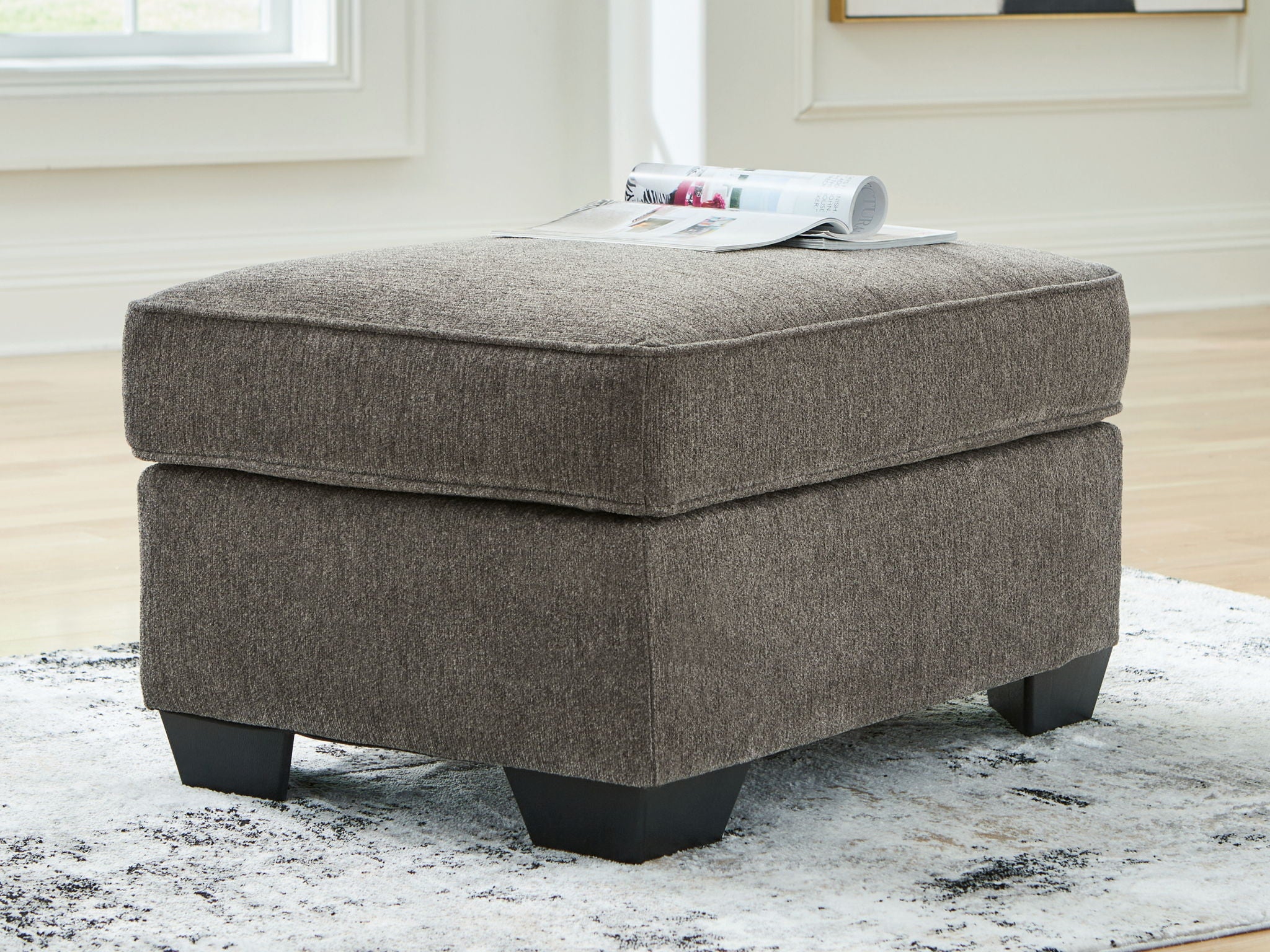 Dark gray upholstered ottoman with cushioned lid and dark block legs