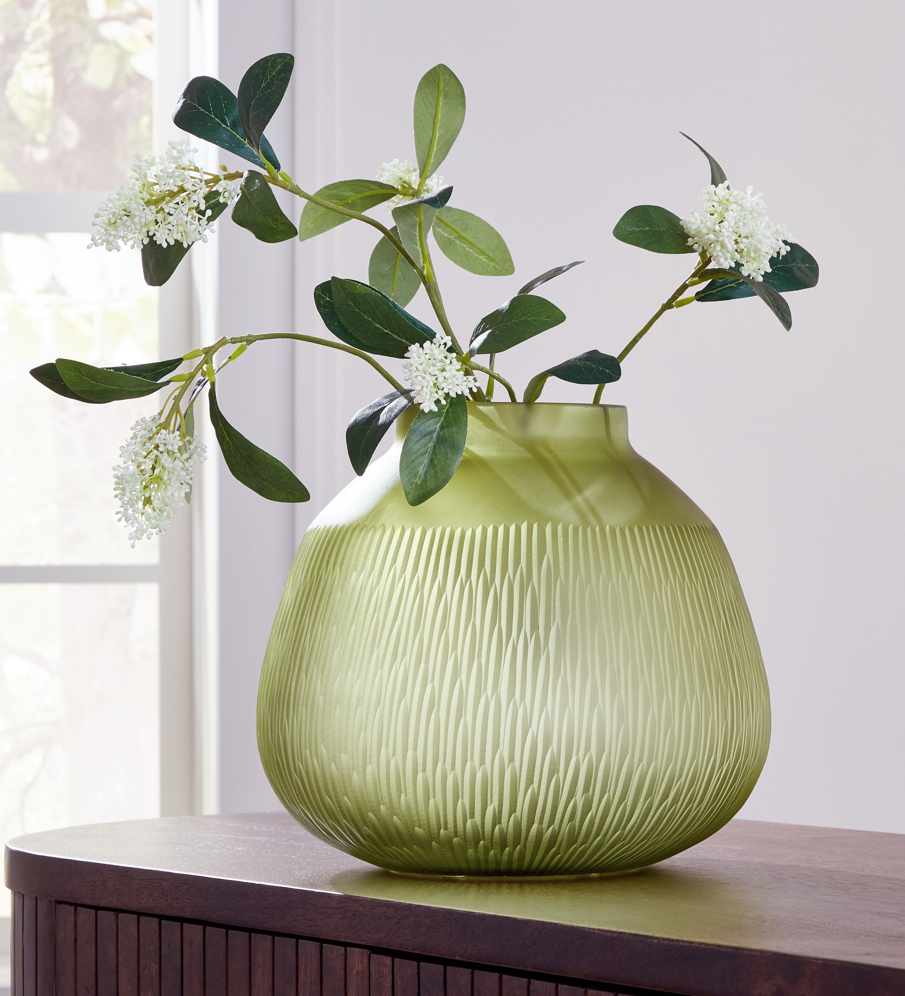 Green glass vase holding white blossoms and green eucalyptus leaves.