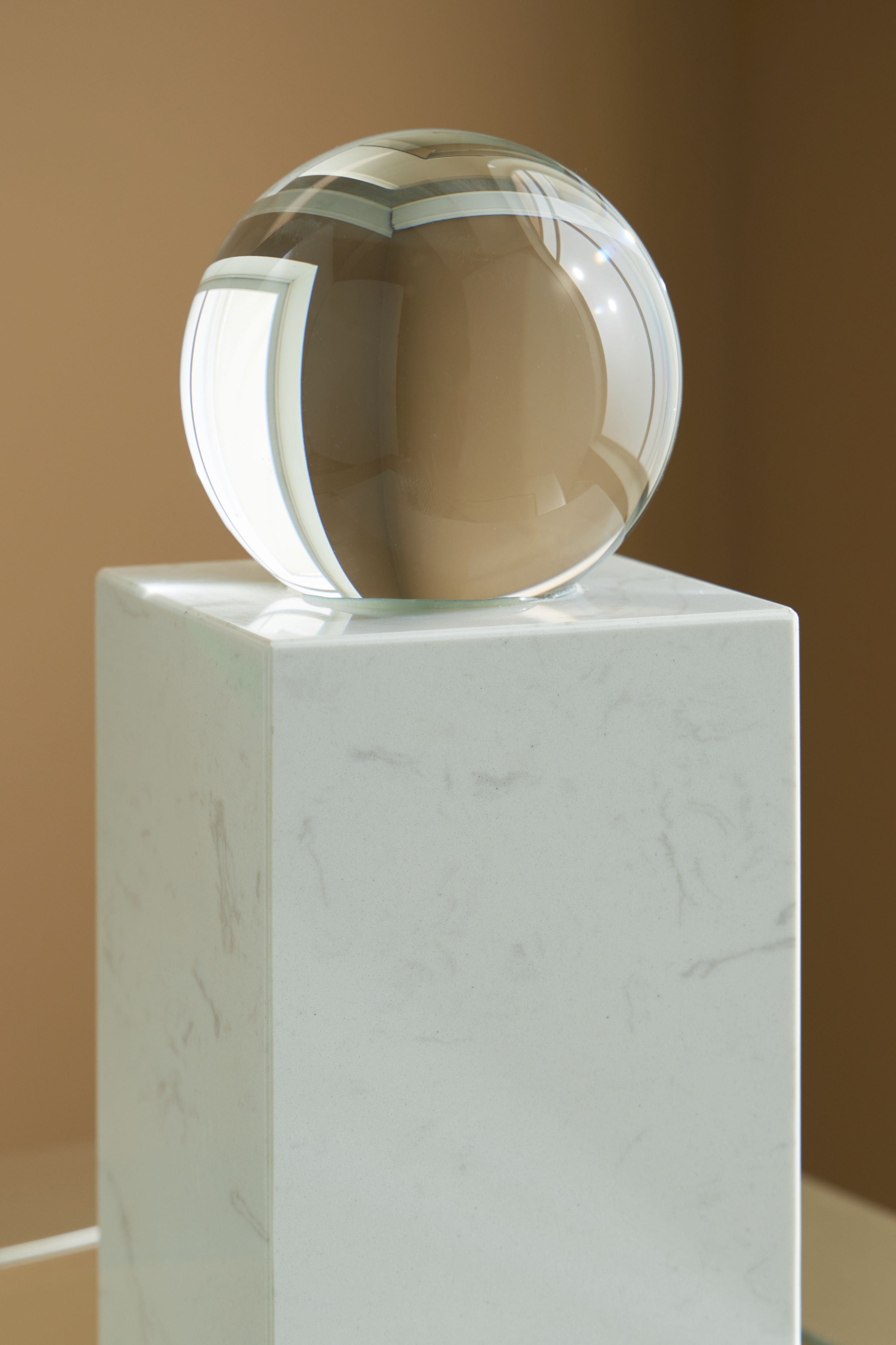 White glass sphere on white marble pedestal, side view
