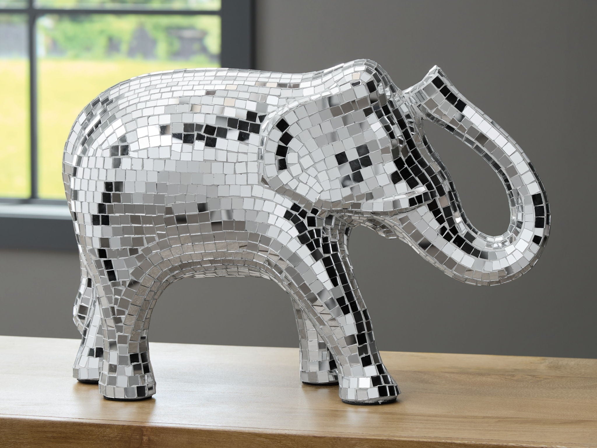 Silver mosaic elephant sculpture on display platform, side view, trunk curved upward