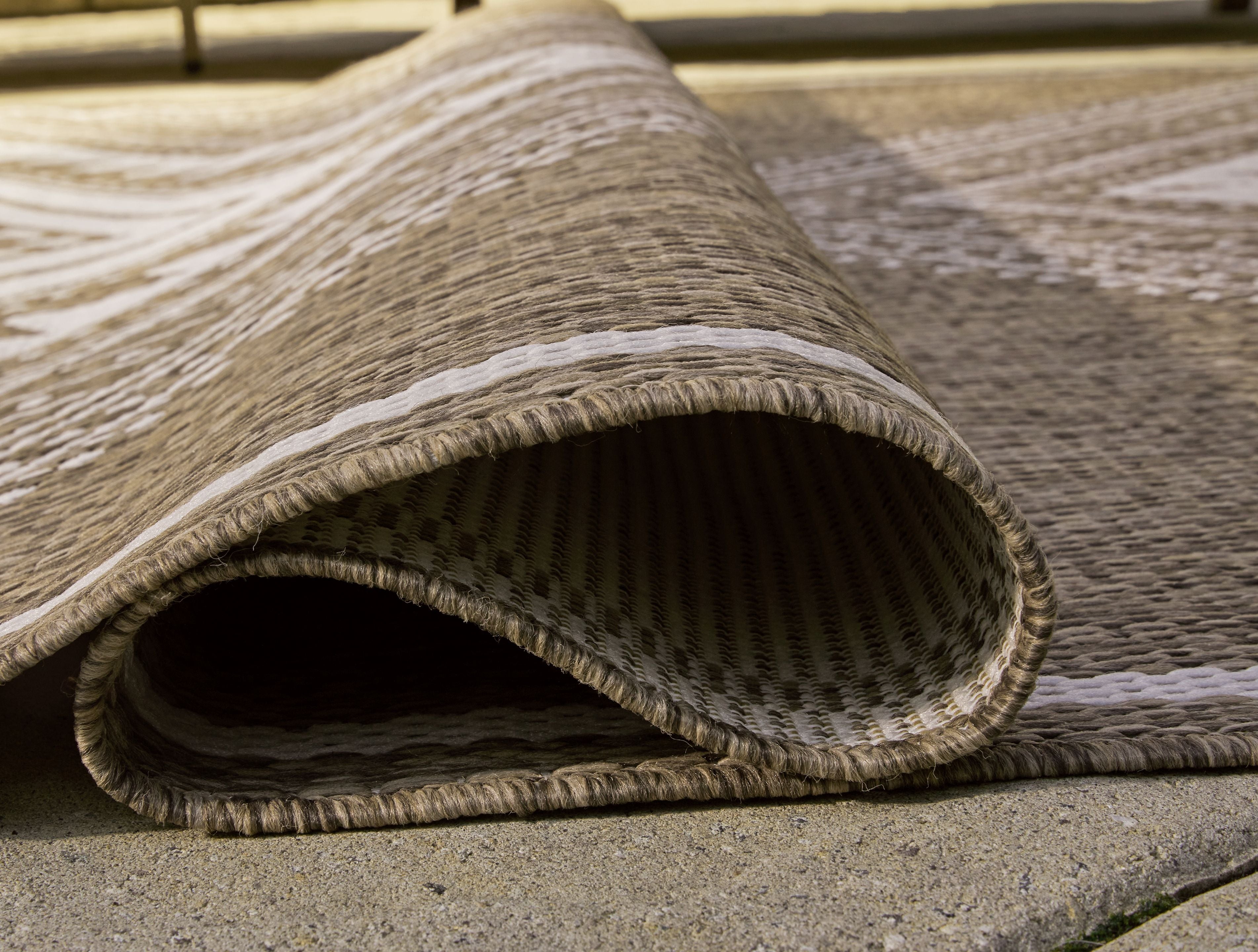 Rolled edge of brown rug with cream geometric stripes and frayed fringe