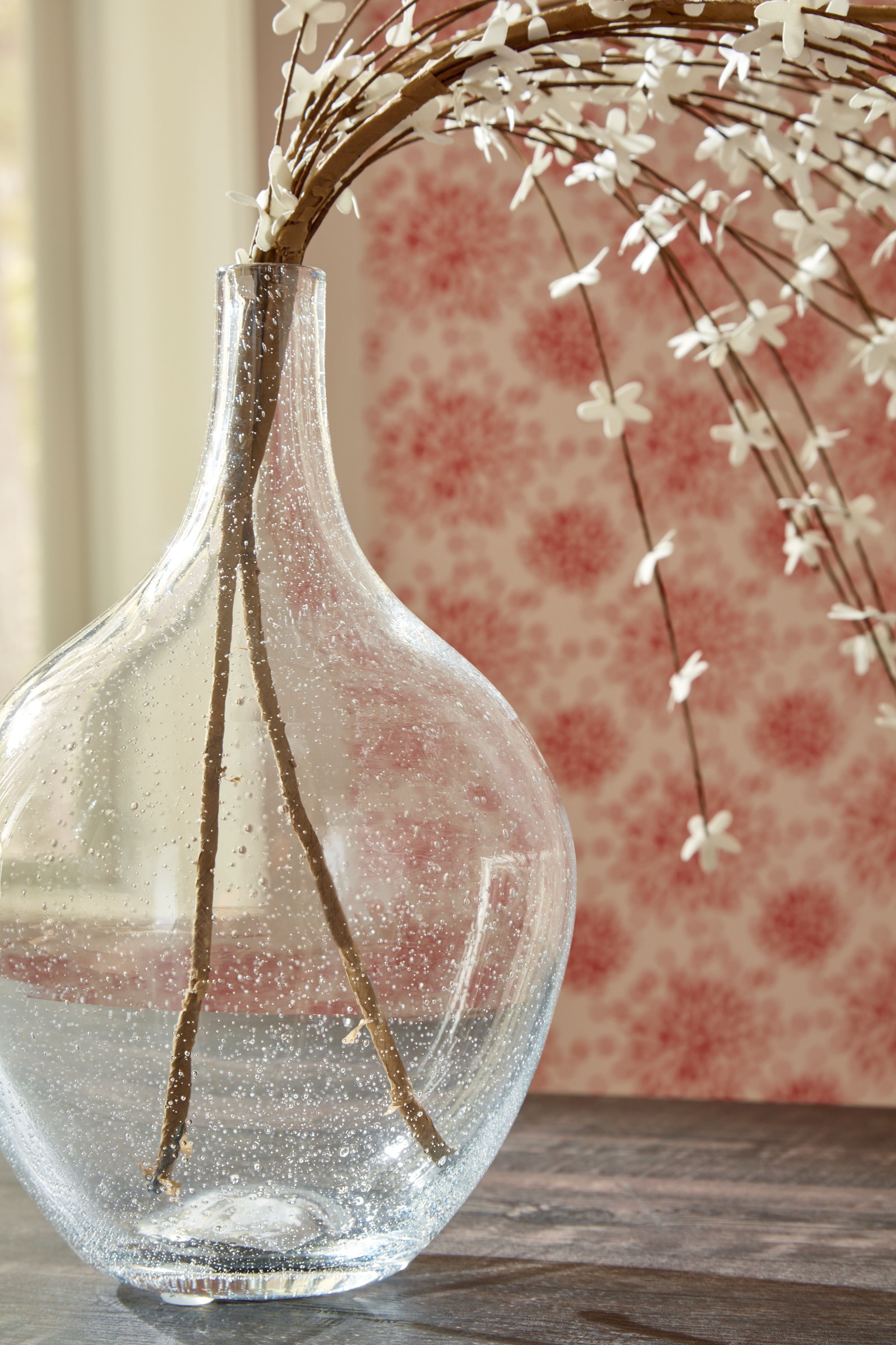 Clear speckled glass vase holding dried stems, narrow neck and rounded base.