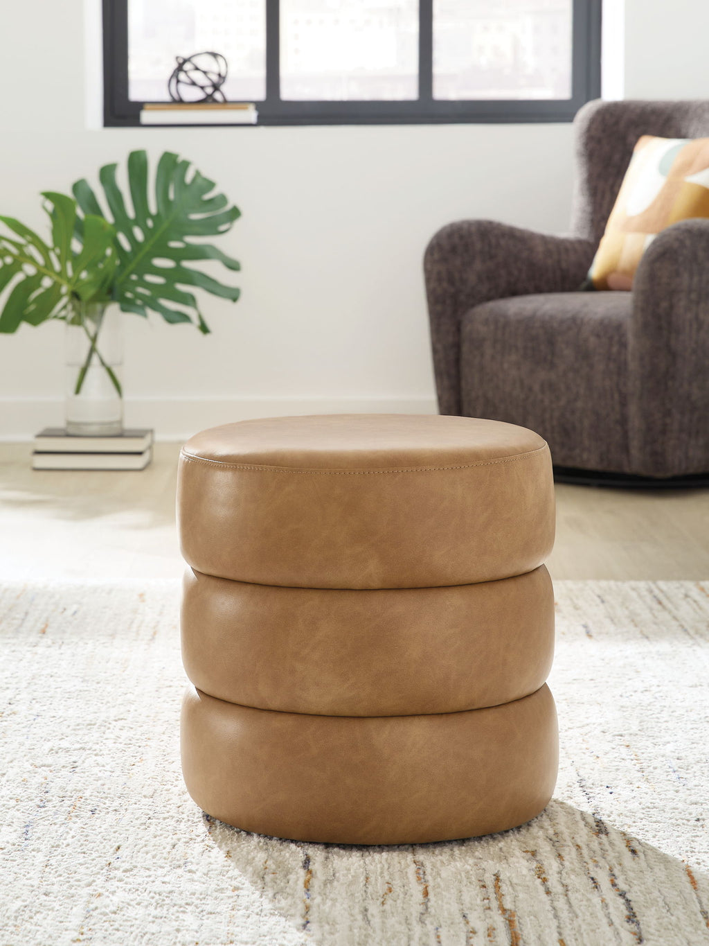 Light brown swivel accent ottoman with round padded top on a stacked upholstered base.