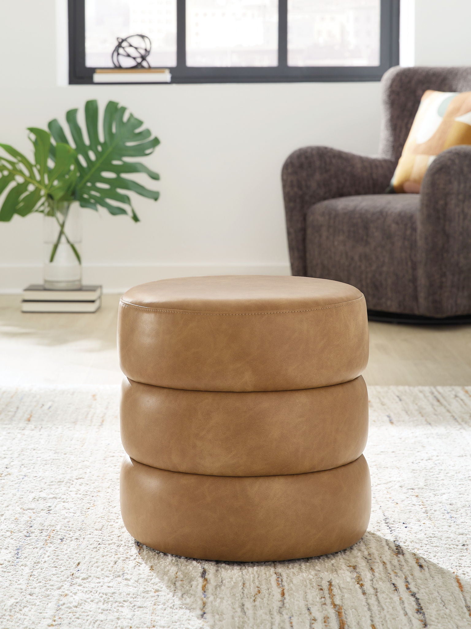 Light brown swivel accent ottoman with round padded top on a stacked upholstered base.