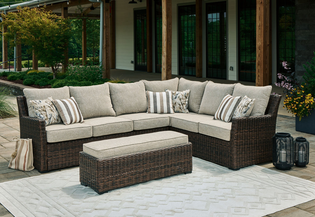 Brown wicker outdoor sectional sofa set with beige cushions, striped pillows, ottoman