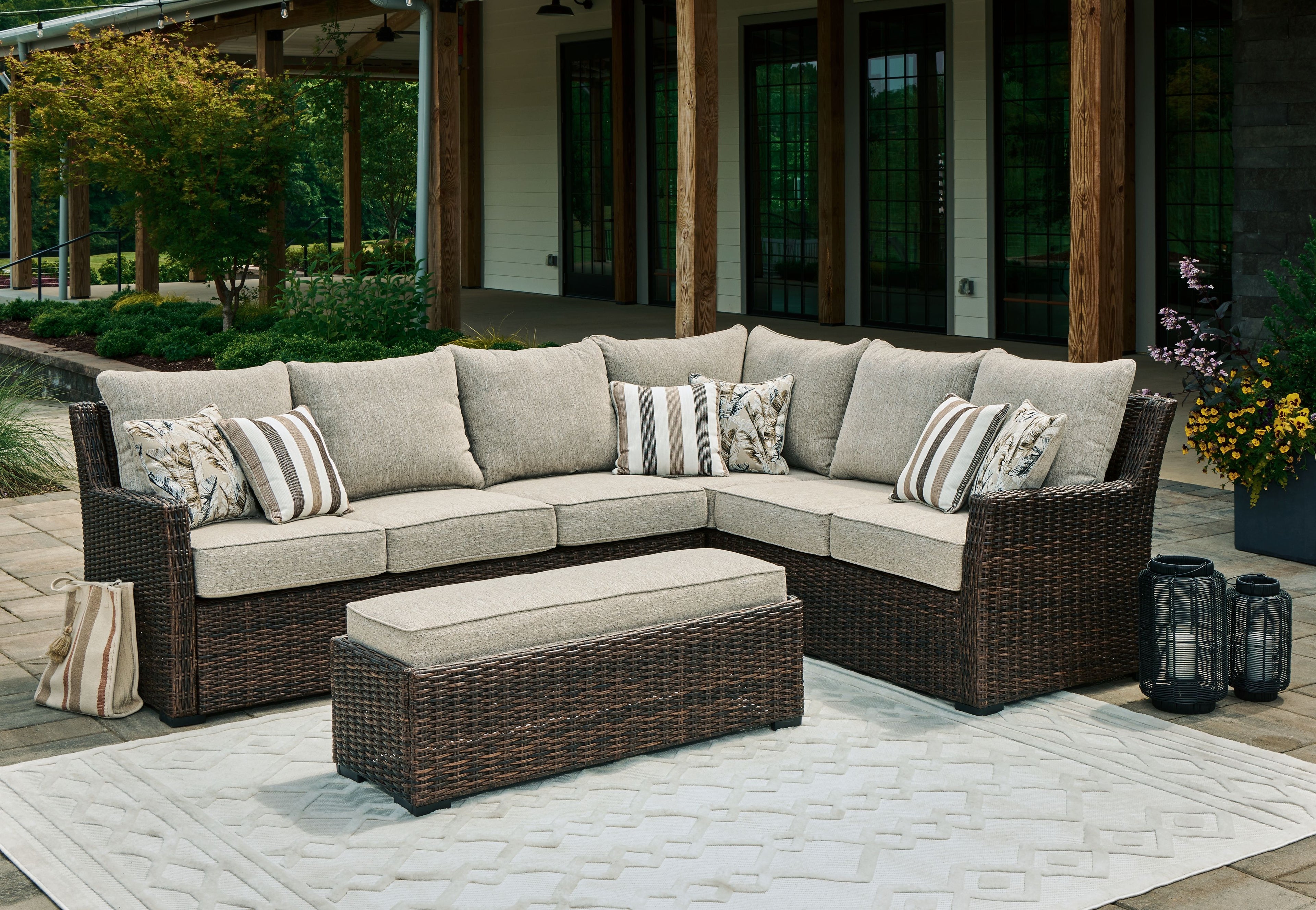 Brown wicker outdoor sectional sofa set with beige cushions, striped pillows, ottoman