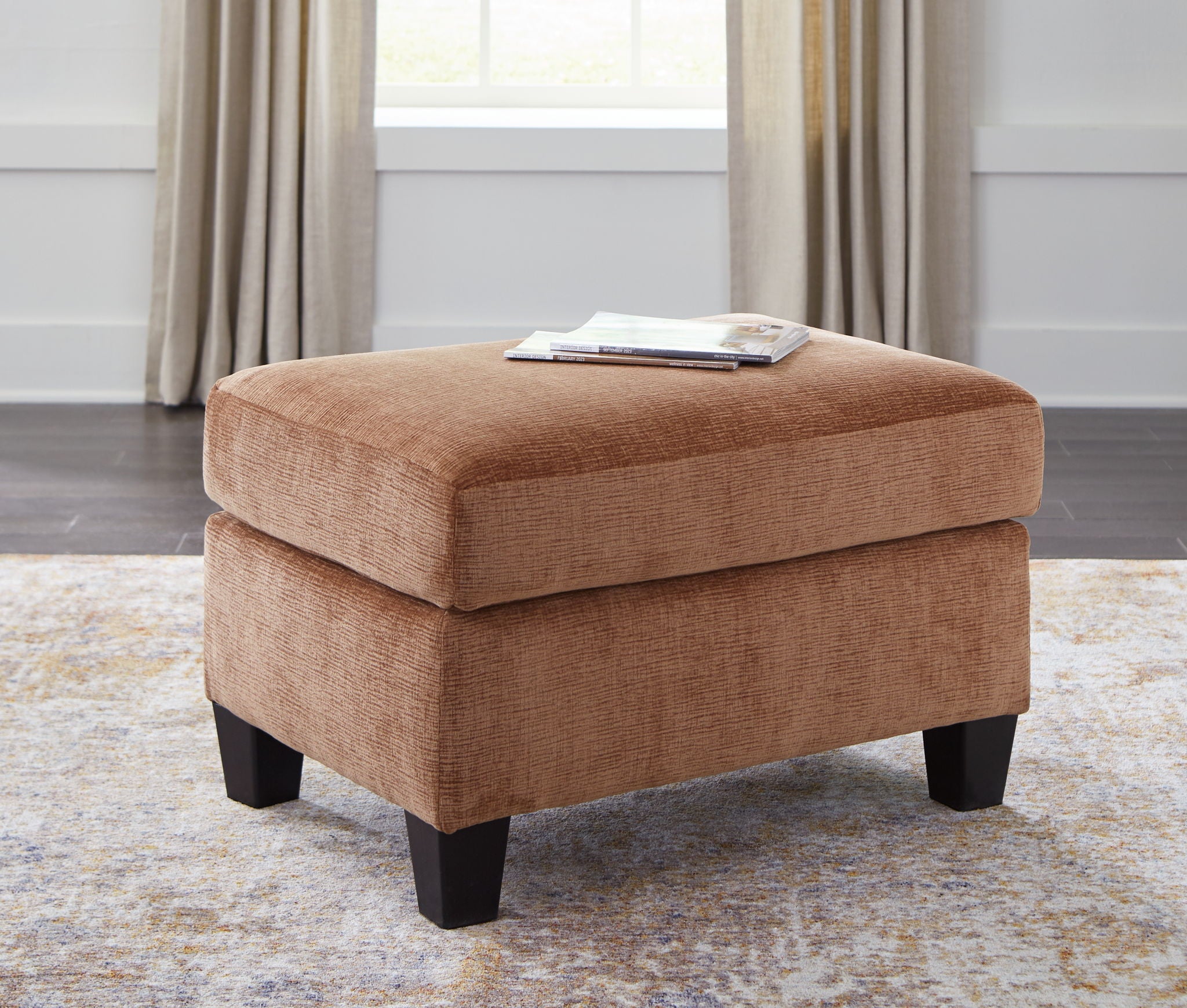 Upholstered clay ottoman with cushioned top and dark legs for seating or footrest