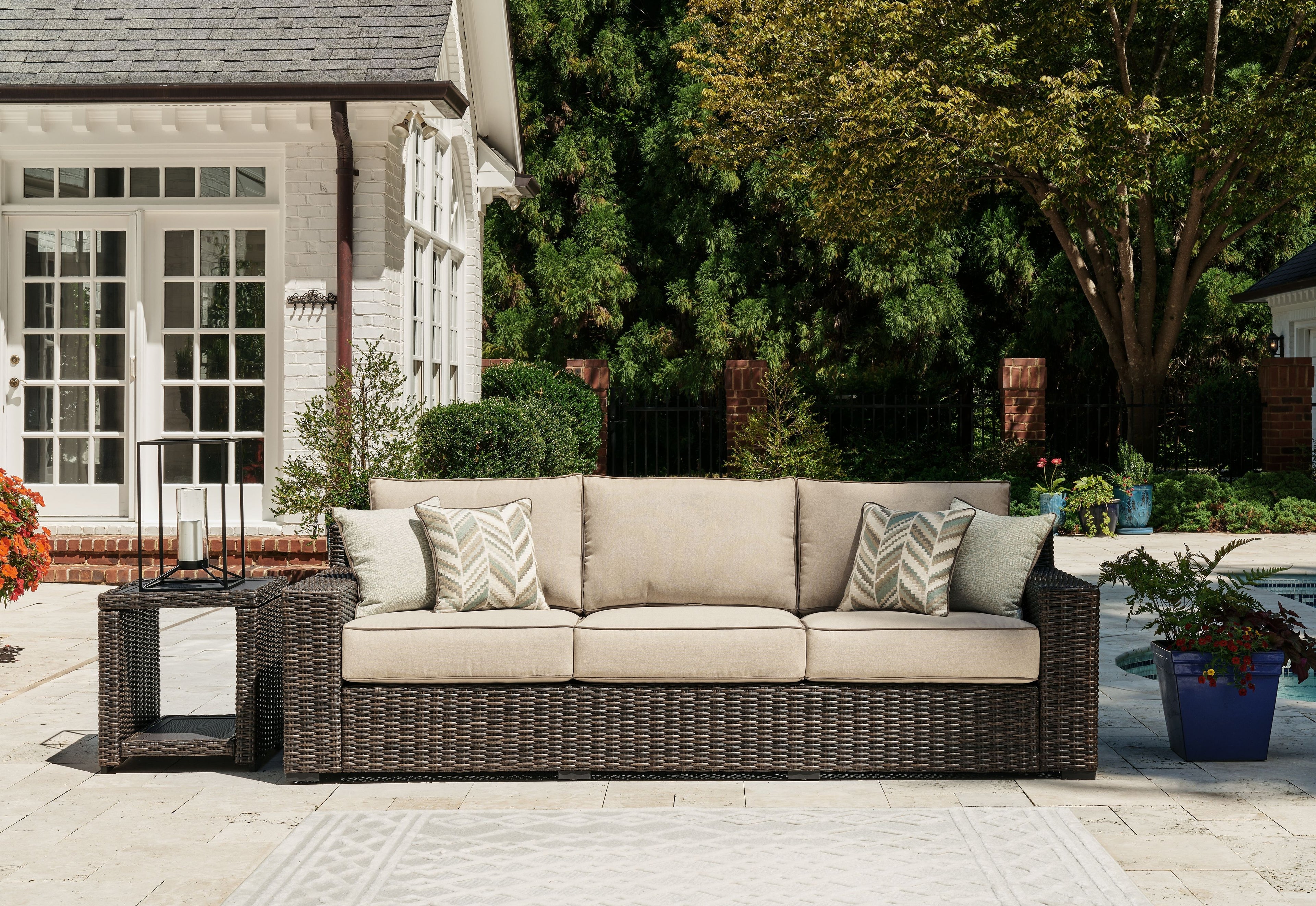 Brown wicker outdoor sofa with beige cushions and two patterned throw pillows