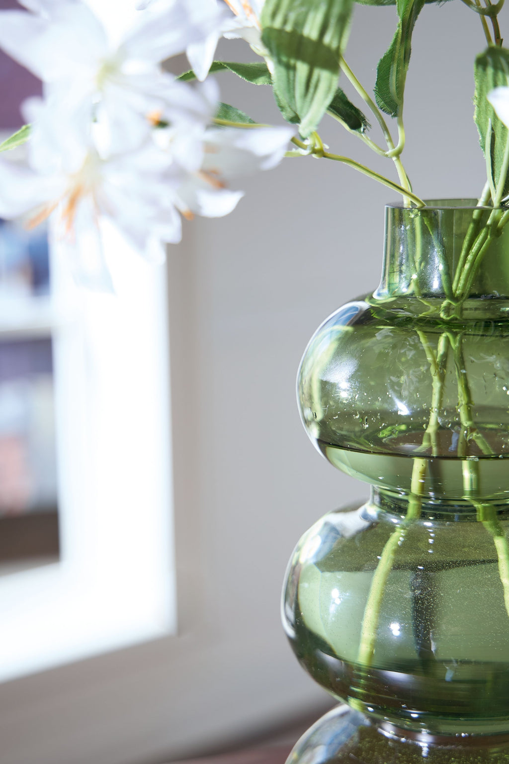 Green glass vase with stacked rounded shapes and visible stems through the opening.