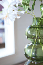 Green glass vase with stacked rounded shapes and visible stems through the opening.