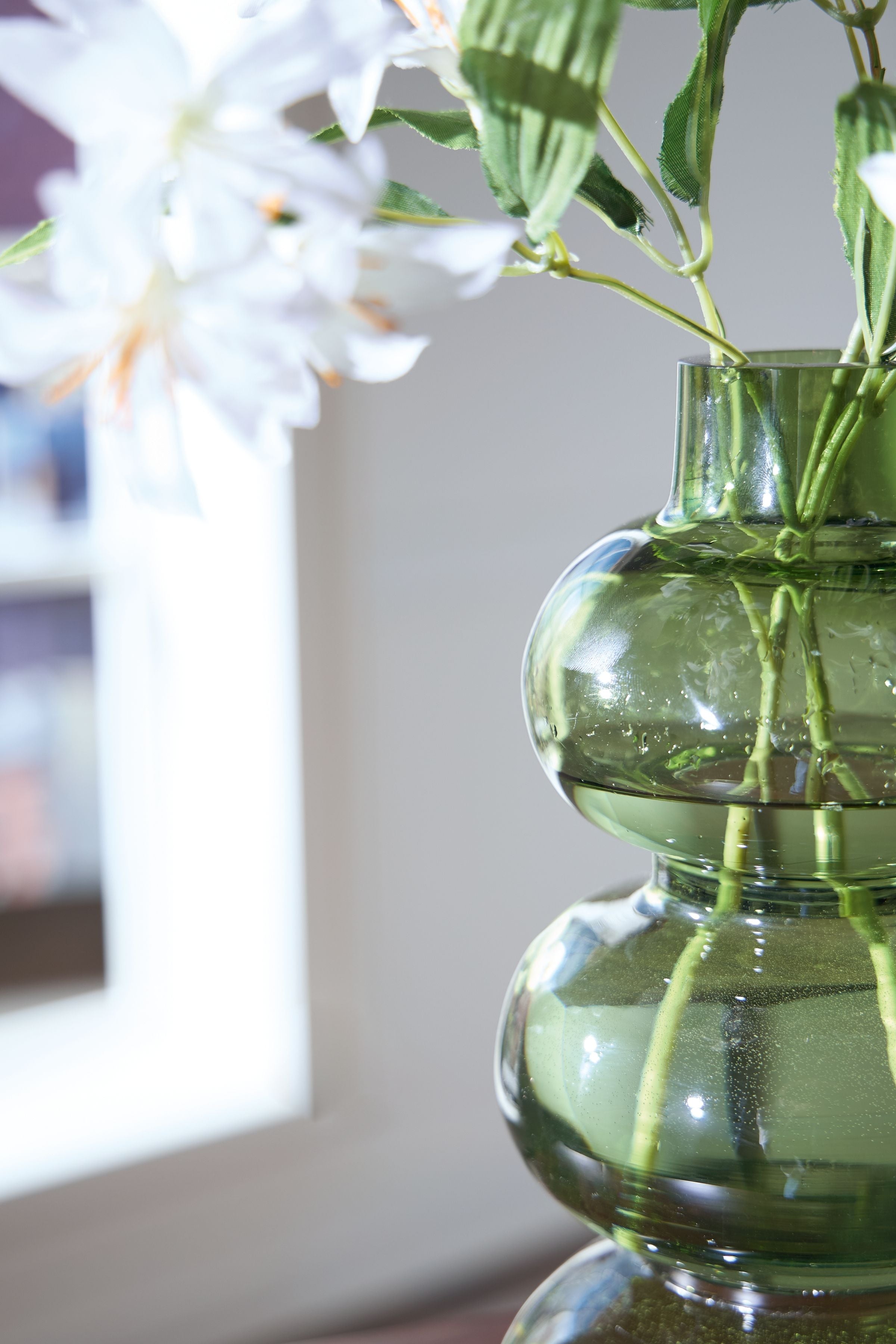 Green glass vase with stacked rounded shapes and visible stems through the opening.
