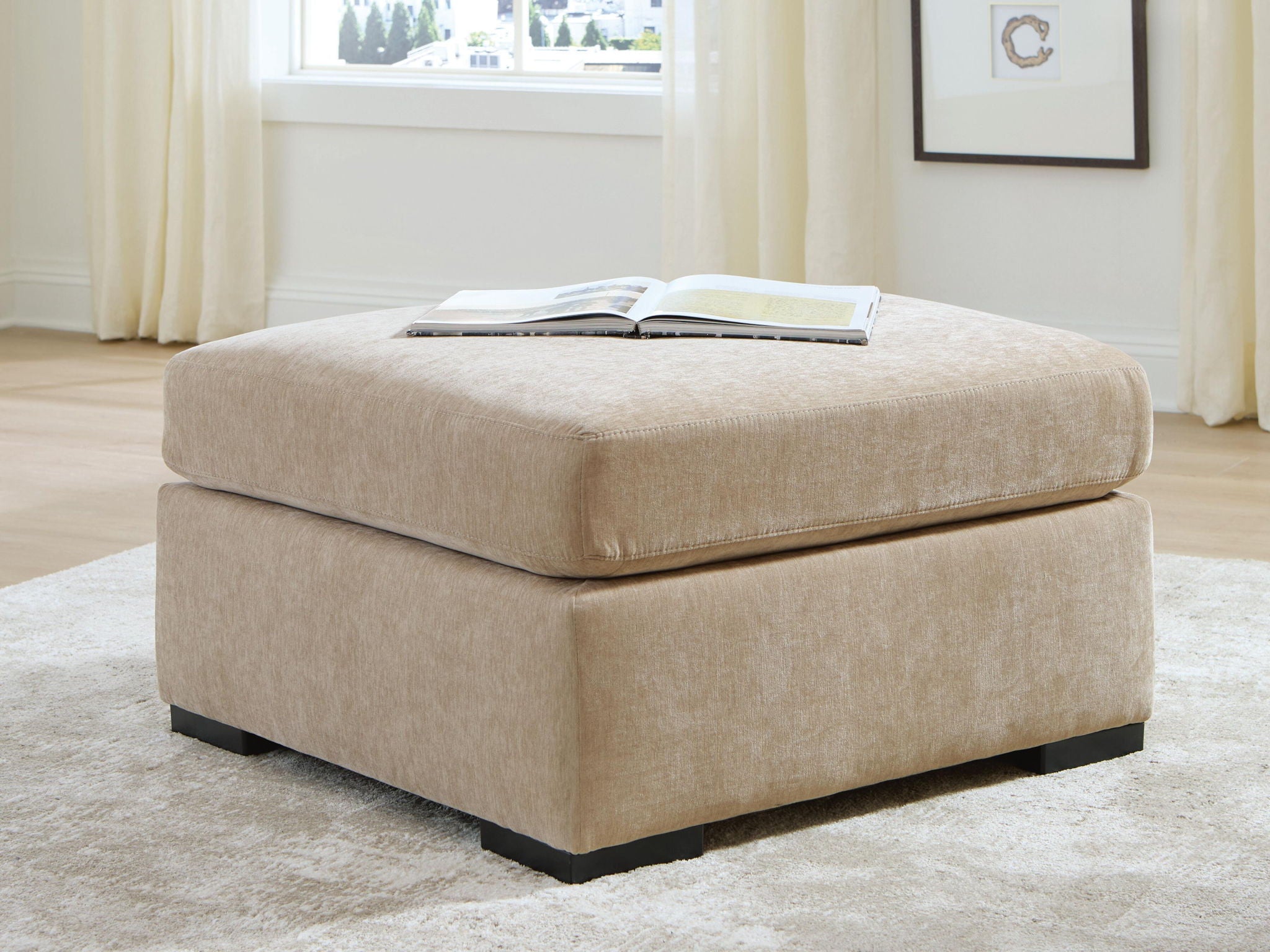 Light brown upholstered oversized accent ottoman with black legs and flat top cushion