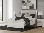White upholstered panel bed with padded headboard, layered pillows, and a dark throw blanket