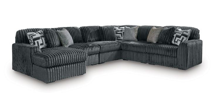 Dark charcoal sectional sofa with corner chaise and geometric-pattern throw pillows on arms.