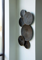 Black and gold circular wall decor with five metal discs arranged vertically on wall