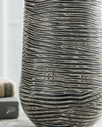 Ceramic vase close view in dark gray with light wavy horizontal etched lines.