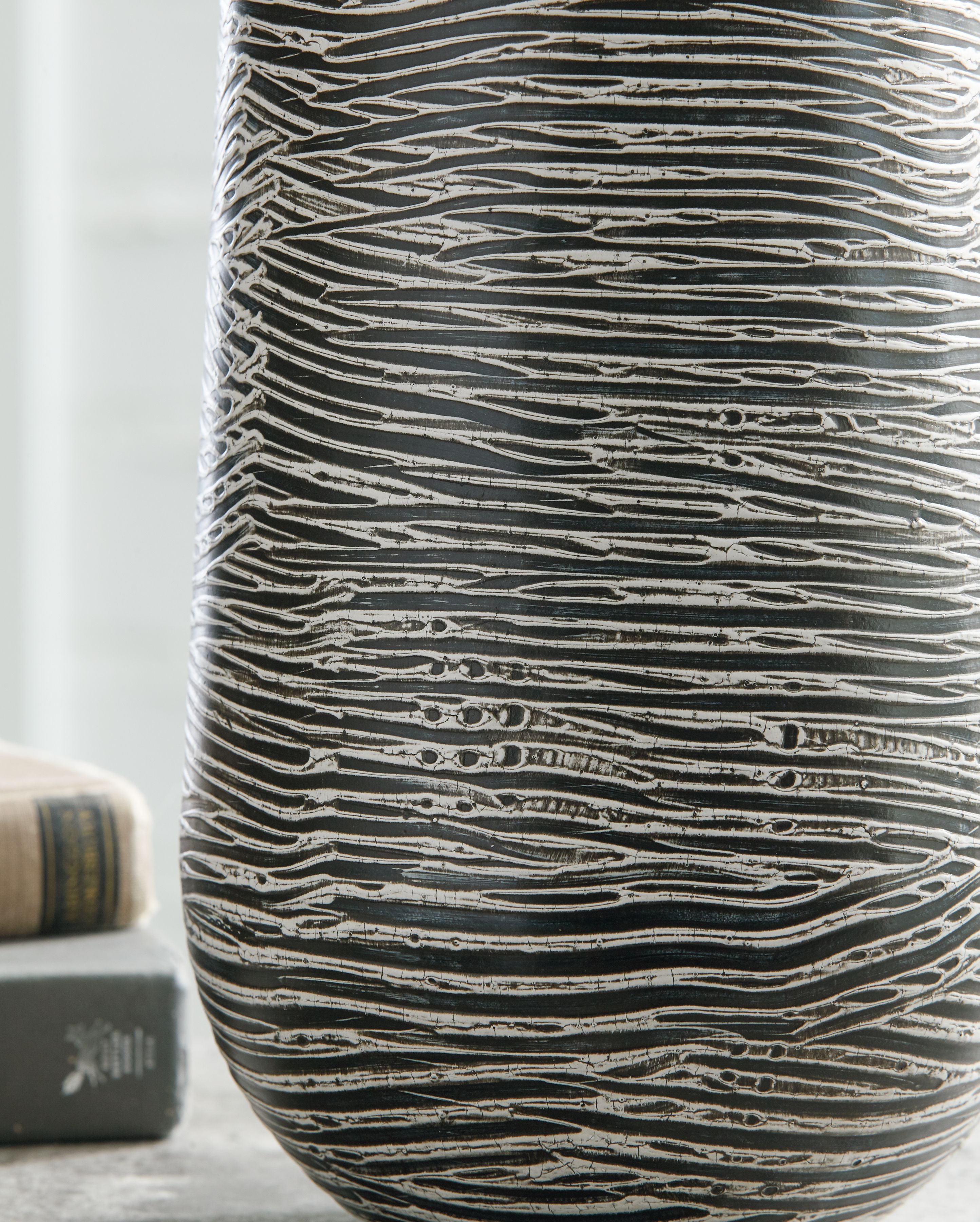 Ceramic vase close view in dark gray with light wavy horizontal etched lines.