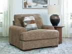 Armchair in light brown fabric with wide arms and attached seat cushion, plus two throw pillows