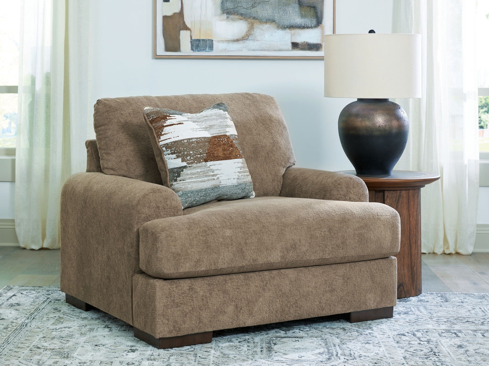 Armchair in light brown fabric with wide arms and attached seat cushion, plus two throw pillows