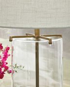 Clear glass lamp body with gold hardware and white fabric shade