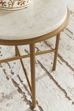 Round table close-up: cream stone-look top edge and gold metal legs over rug.