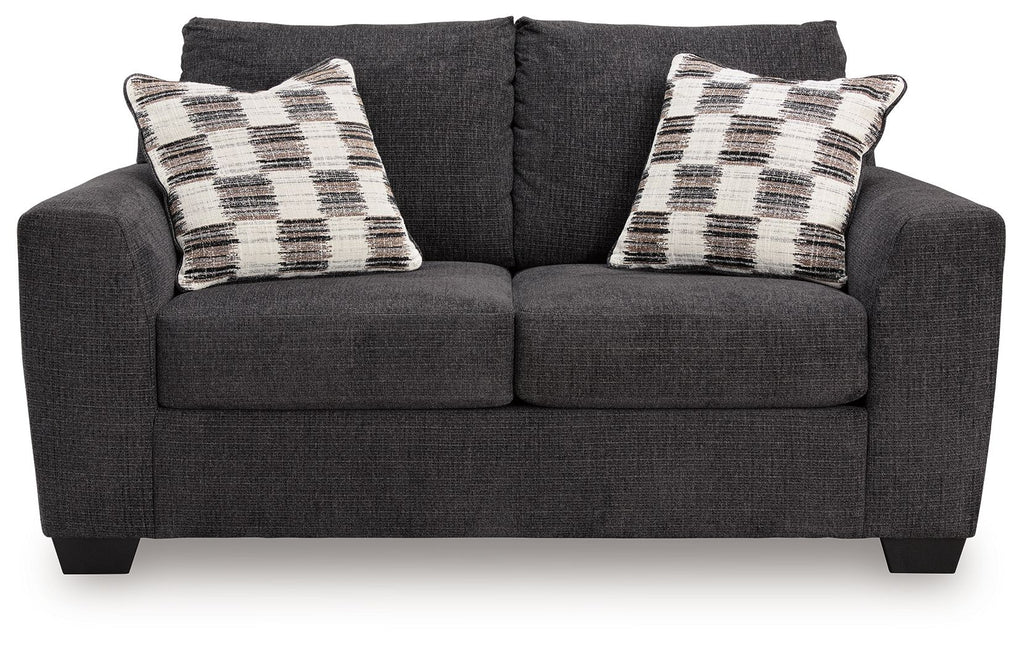Dark gray loveseat with two plaid throw pillows and tufted seat back