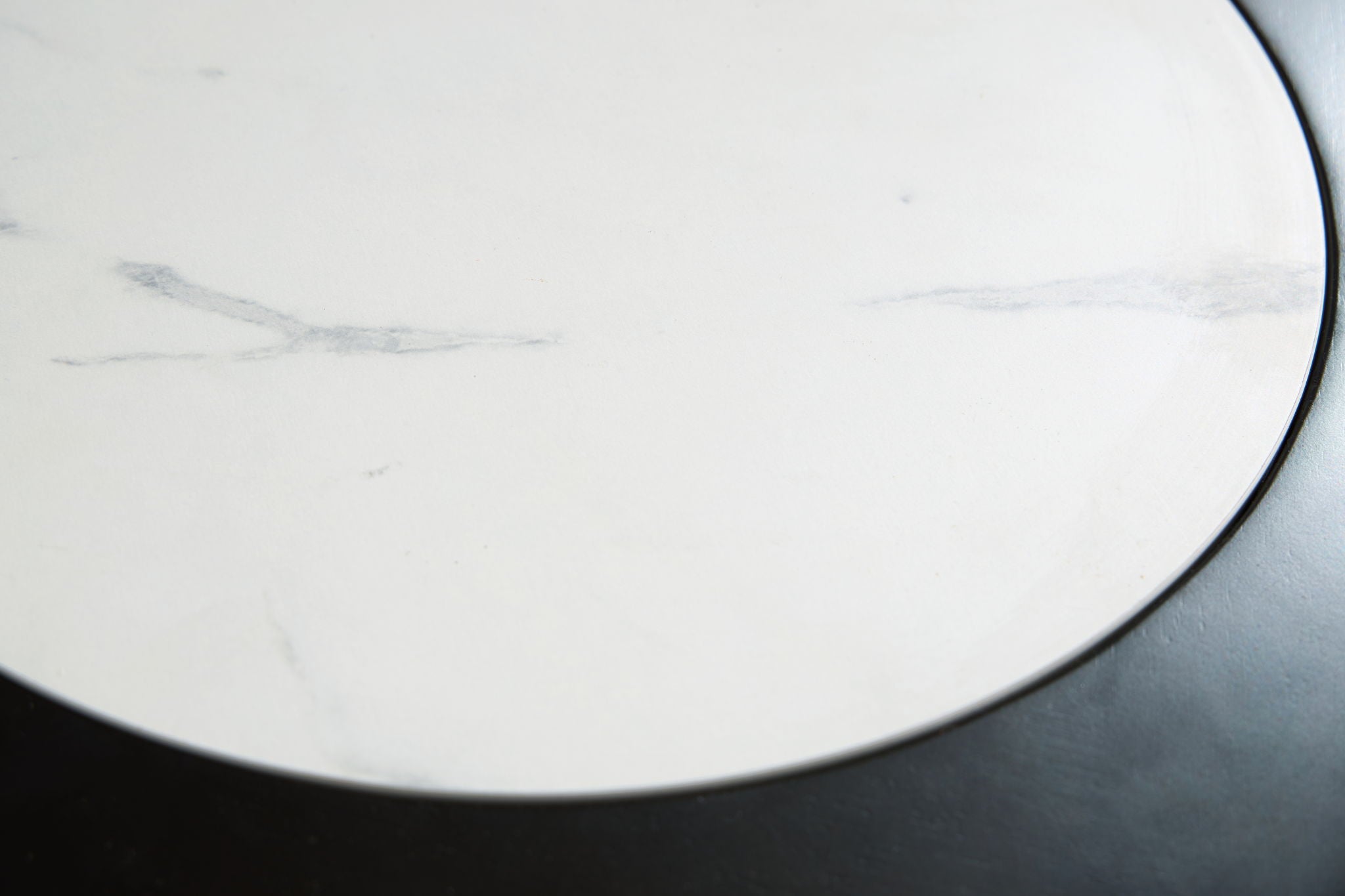 White marble-look tabletop close-up with light gray veining and black rim