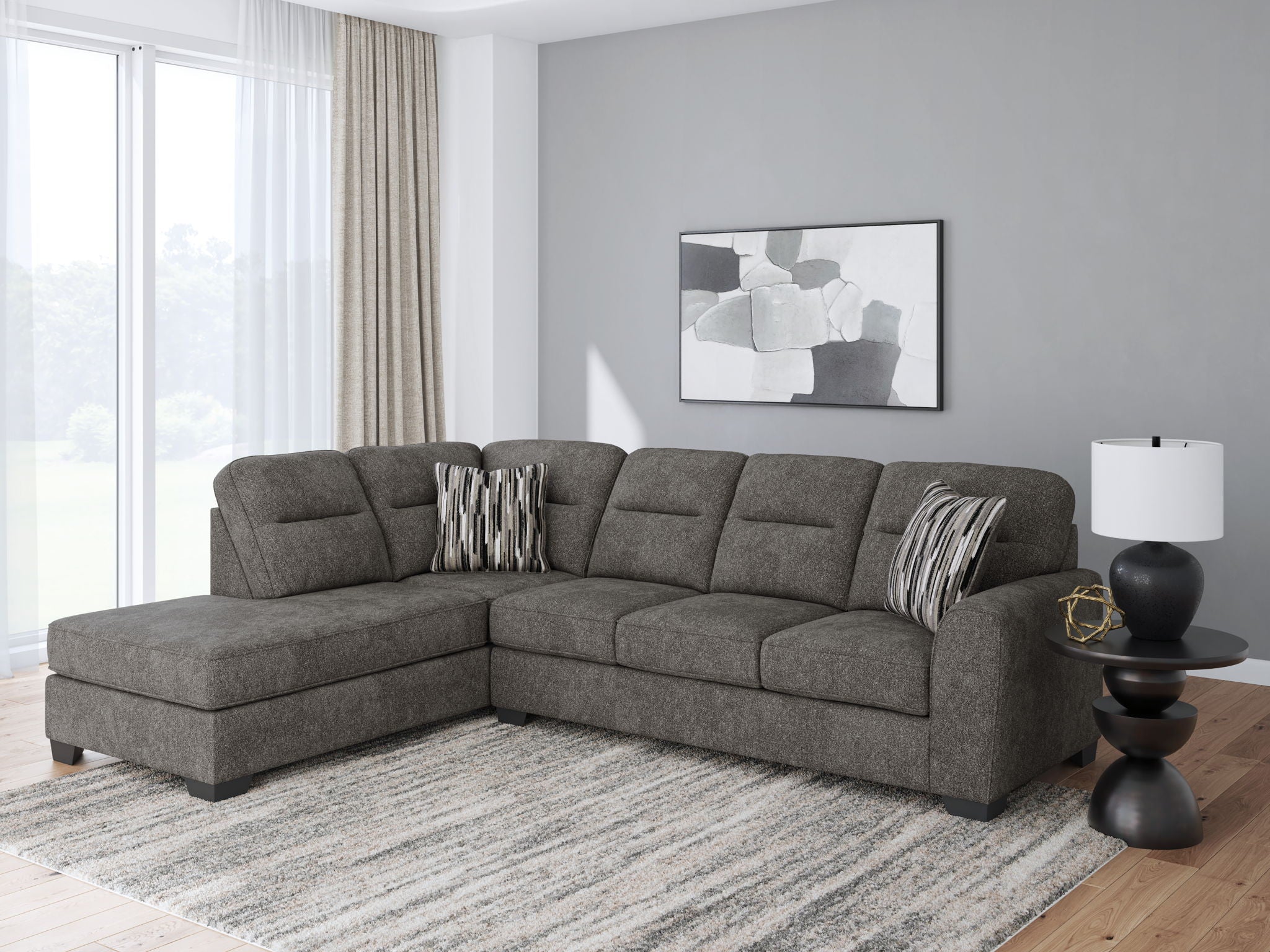 Dark gray sectional sofa with left chaise, tufted back, and striped pillows in a bright room