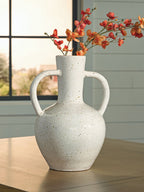 Speckled white ceramic vase holding red flowers, with two loop handles.