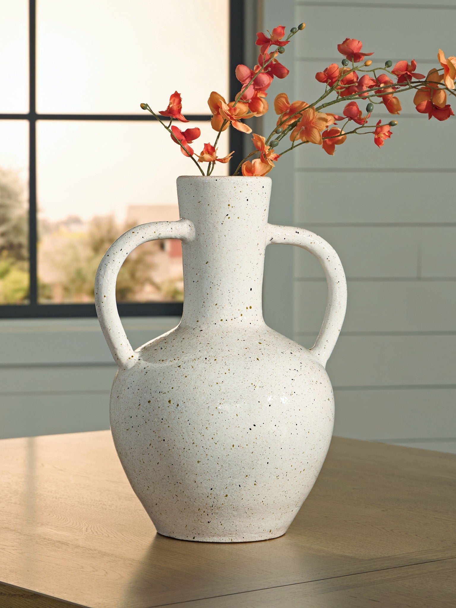 Speckled white ceramic vase holding red flowers, with two loop handles.