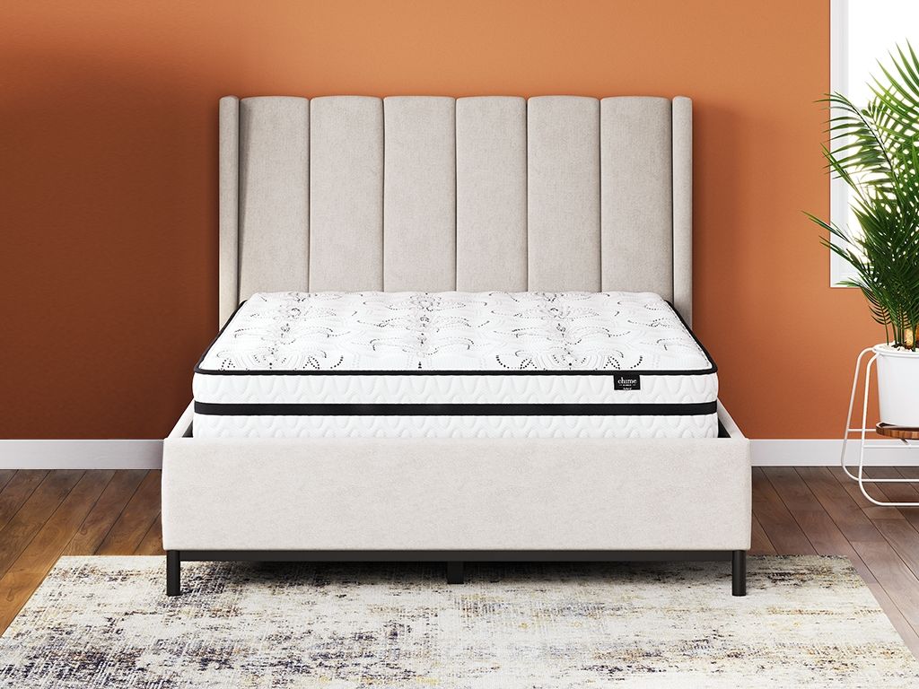 White hybrid mattress on dark platform bed with tufted headboard behind