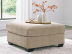 Beige oversized ottoman with ribbed fabric, square padded top, dark legs.
