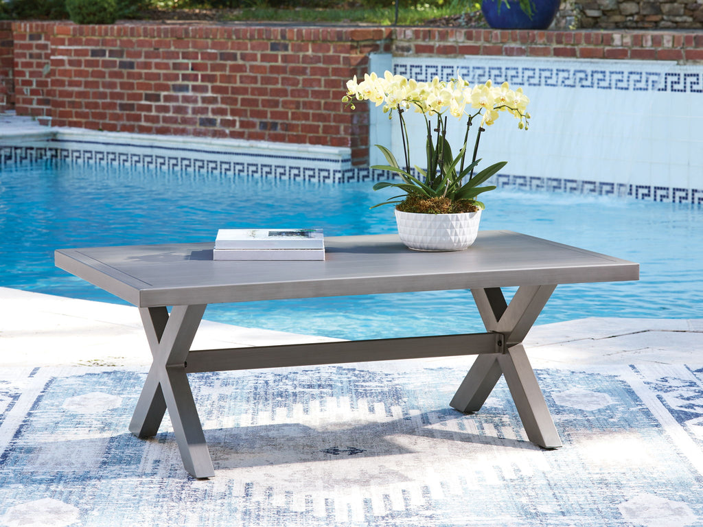 Gray rectangular cocktail table with cross legs, set outdoors.