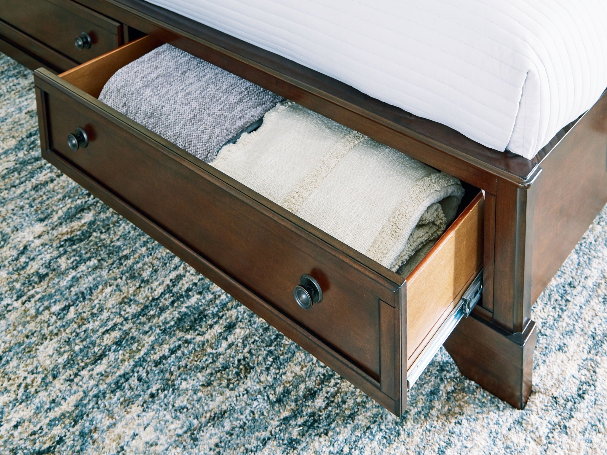 Brown storage bed drawer open on side, showing folded bedding inside