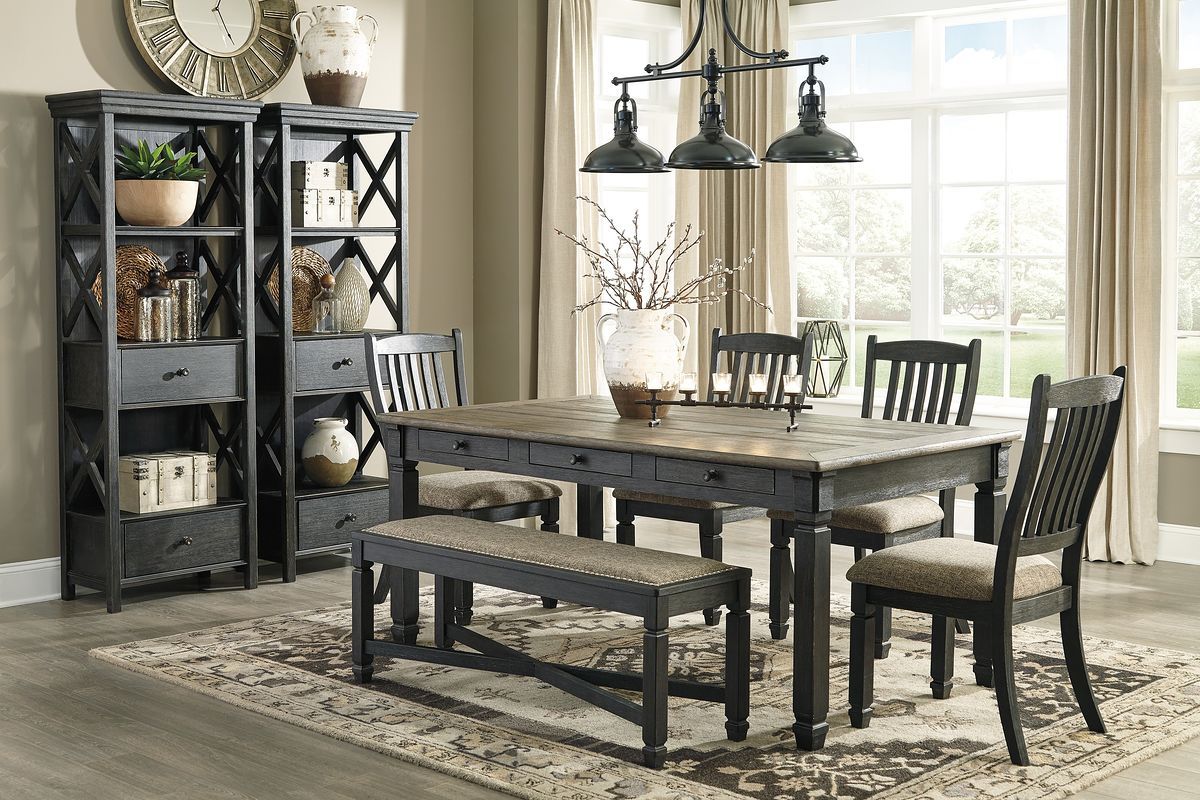 Dark gray dining table with two upholstered benches and four slat-back chairs, bookcase side