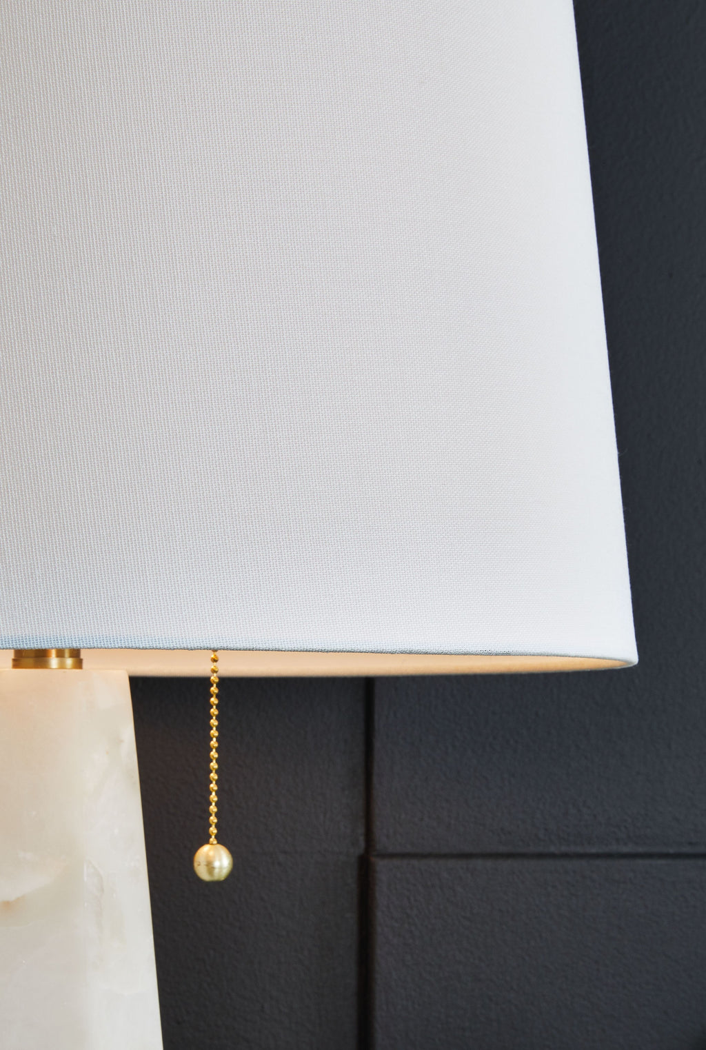 Fabric drum lamp shade with gold pull chain detail on alabaster-style base