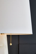 Fabric drum lamp shade with gold pull chain detail on alabaster-style base