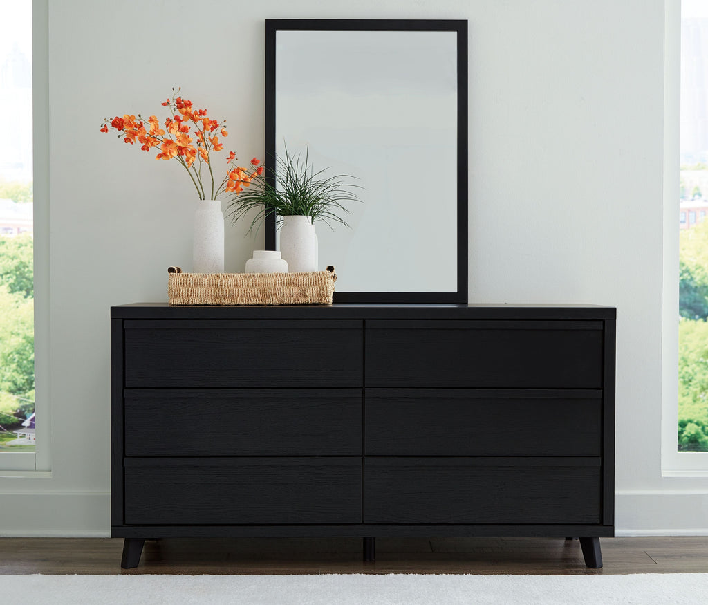 Black dresser with four drawers and tall framed mirror, low legs