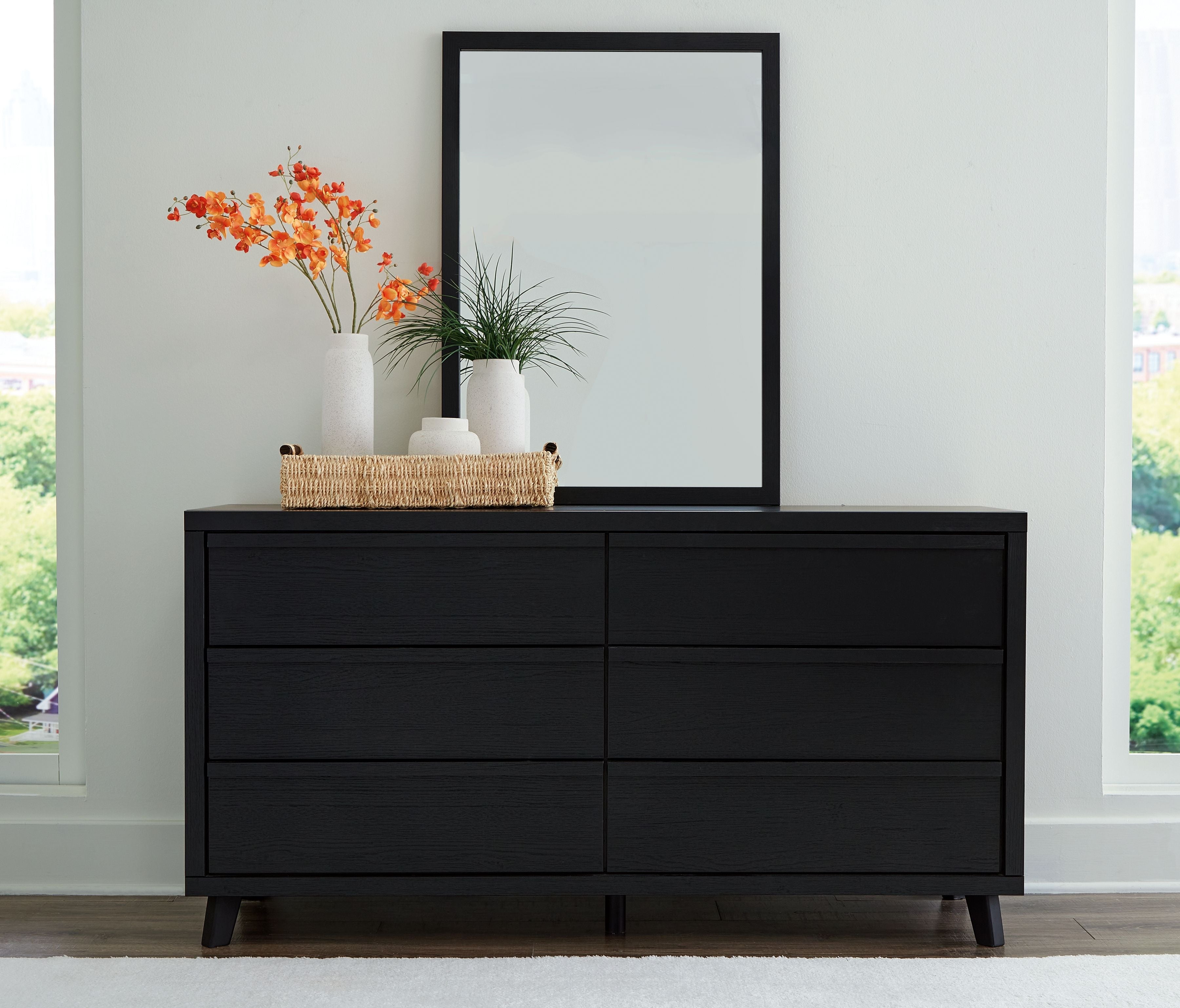 Black dresser with four drawers and tall framed mirror, low legs