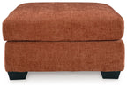 Rust-colored upholstered accent ottoman with square top and dark legs.