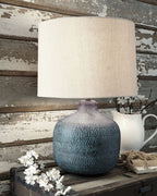 Table lamp with teal metal patina base and off-white drum shade on tabletop