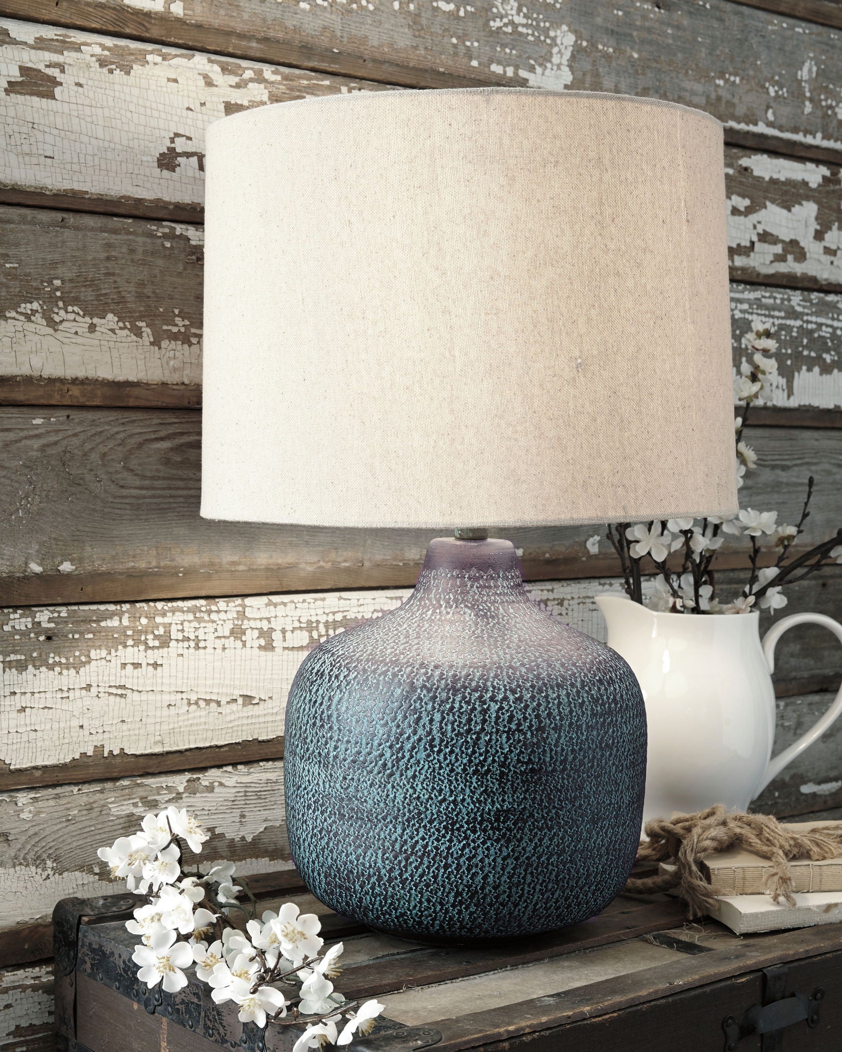 Table lamp with teal metal patina base and off-white drum shade on tabletop