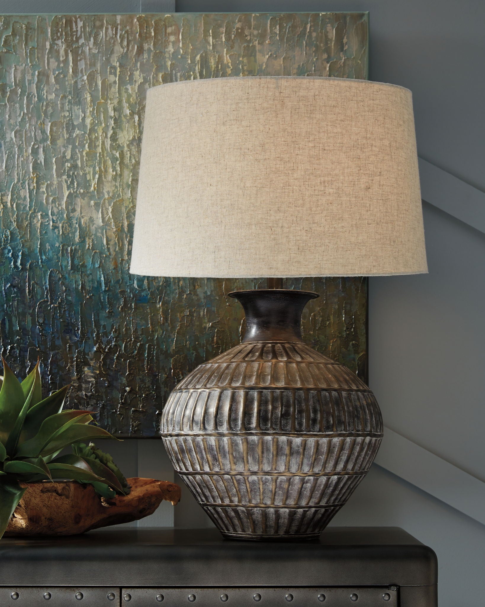 Antique bronze metal table lamp with ribbed urn base and beige drum shade, side view.