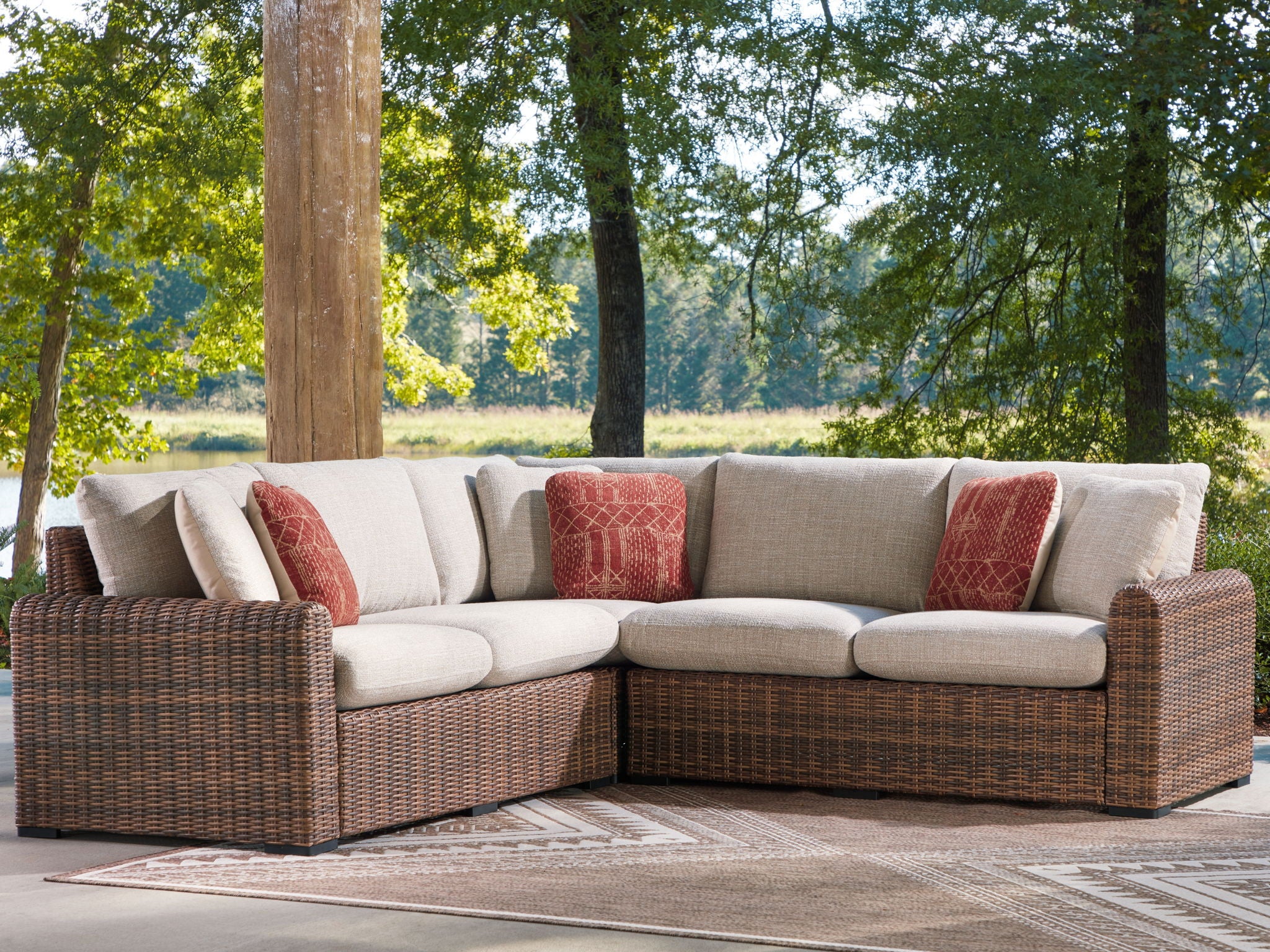 Outdoor sectional sofa with beige cushions, brown wicker sides, and rust patterned pillows