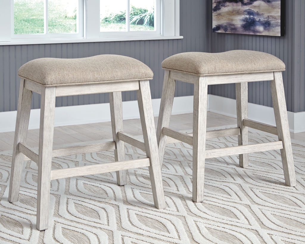 Two weathered gray barstools with beige padded seats on a patterned rug