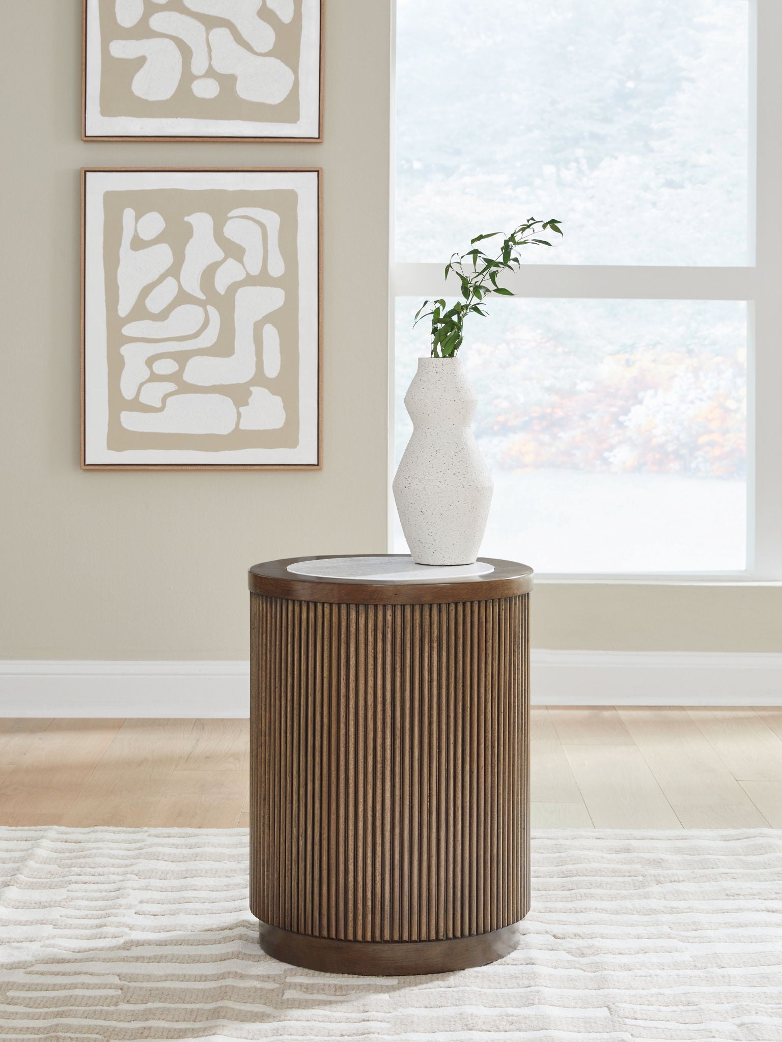 Round side table with slatted light brown sides and gray top, with a white vase.