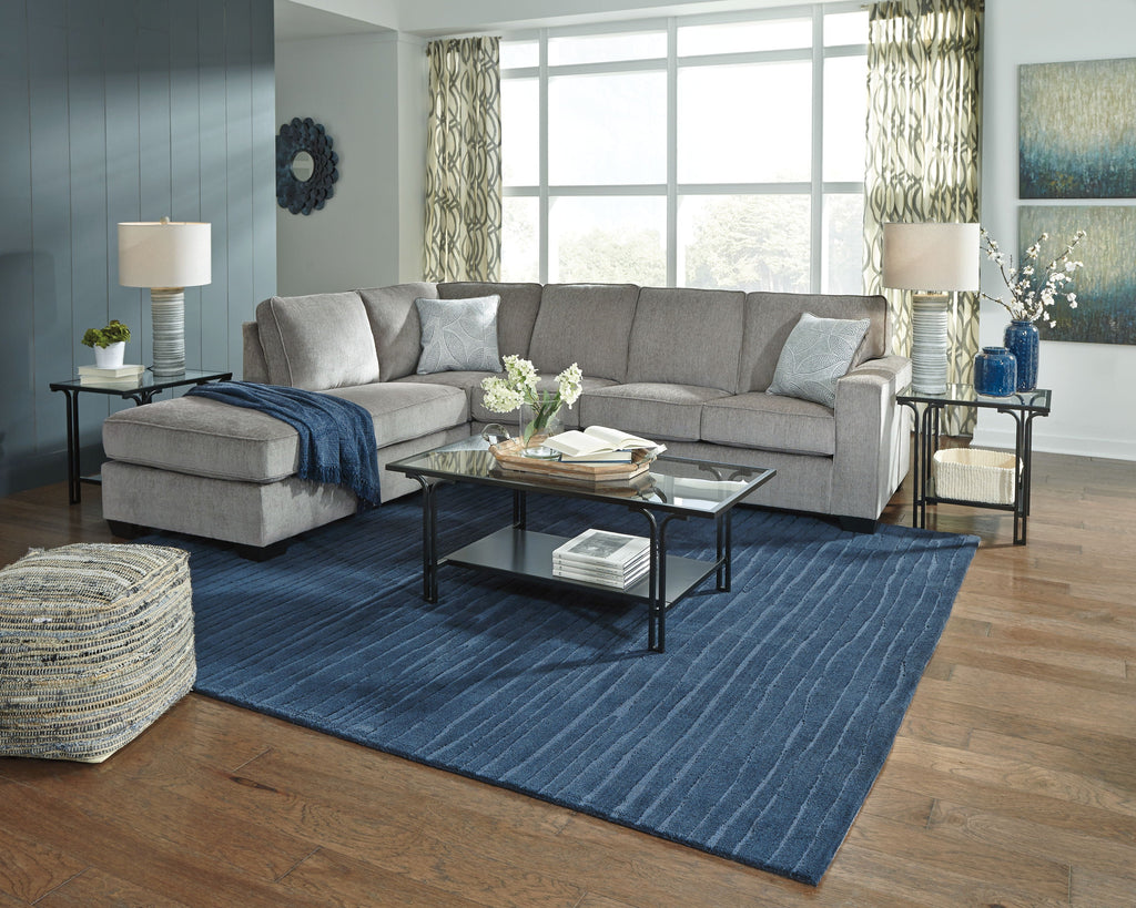 Light gray sectional sofa with chaise and blue throw, tufted seat cushions and back pillows